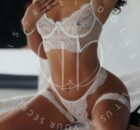 Woman modeling white lace lingerie (bra, garter belt) posing on a bed with jewelry.