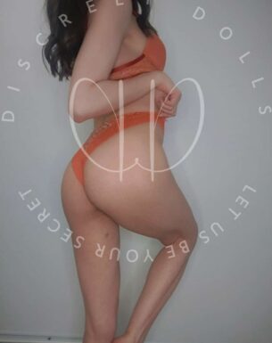 Side profile of a woman wearing orange lace lingerie, standing with arms crossed over her torso and visible lower body.