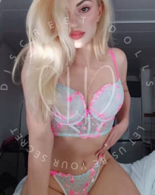 Woman wearing pastel lace lingerie posing on a bed, facing the camera.